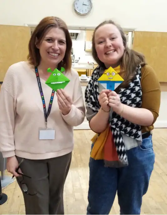 Two smiling ladies holding up origami